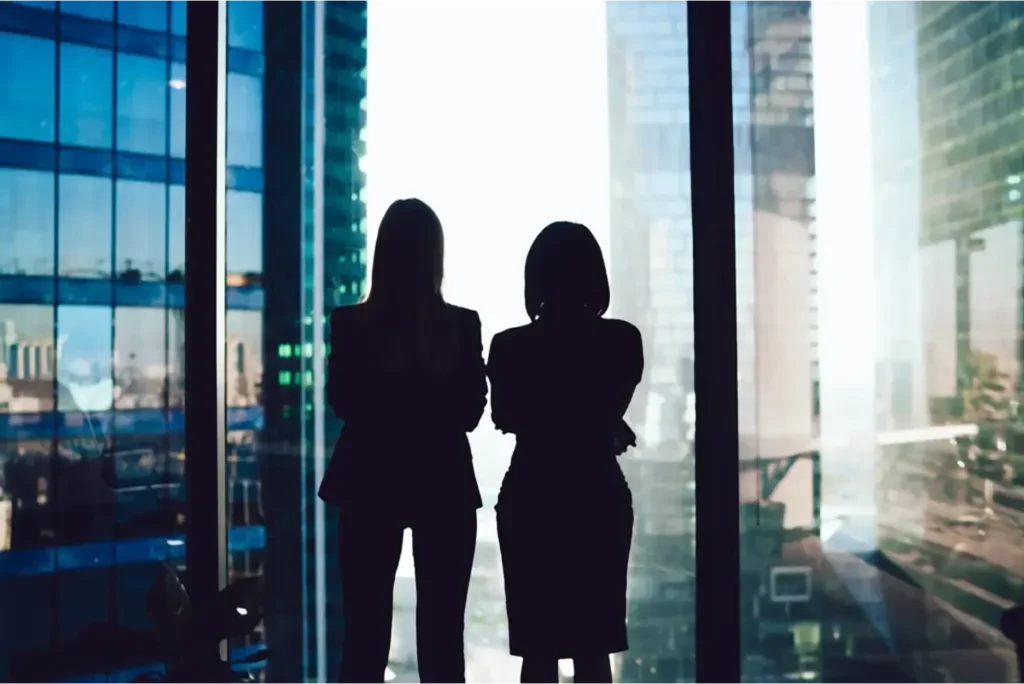 Two businesswomen look out the window of an office tower