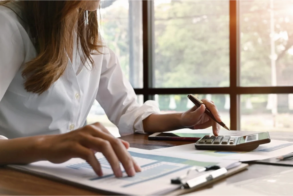 A woman sitting at a desk, using a calculator and checking a chart
